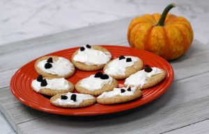 crackers with cream cheese and raisins on red plate with pumpkin in background