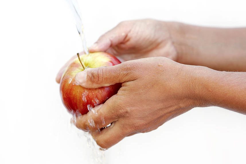 Hands washing a red apple under running water.