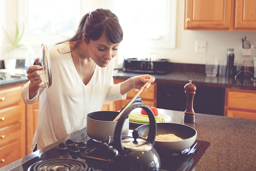 Woman cooking in the kitchen smelling something in a pot on the stove.