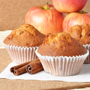 muffins in paper cups with cinnamon sticks and apples in background