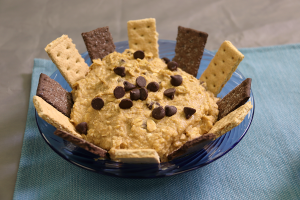 graham crackers in hummus topped with chocolate chips in a blue bowl on a blue placemat