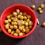 roasted chickpeas spilling out of a red bowl onto a brown background