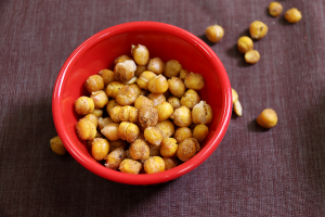 roasted chickpeas spilling out of a red bowl onto a brown background