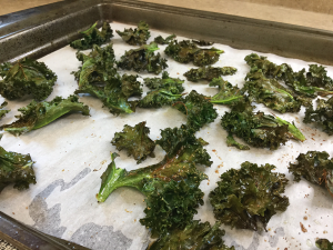 Crisped kale chips laid on parchment paper on a metal cookie sheet