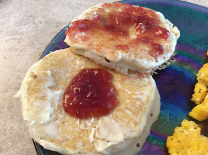 two round pancakes covered in butter and strawberry jelly next to scrambled eggs on a blue plate