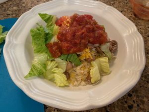 pinto beans and brown rice on a white plate paired with salsa, lettuce, and cheese