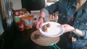 3 peanut butter balls on a white plate held by a woman's hands in a kitchen with recipe ingredients and cookbook in the background