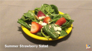 Prepared salad on yellow plate resting on brown background with white text "Summer Strawberry Salad"