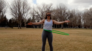 blond girl with arms out uses green hula hoop in park with grass