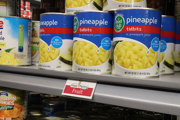 Cans of pineapple on a grey metal shelf with a sign below reading 'fruit'