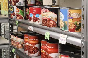 Cans of various beans on a grey metal shelf with signs below reading 'beans', 'chili beans', and 'vegetarian'.