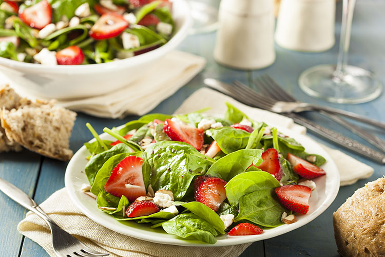 Strawberries, spinach, and almonds in a white bowl on a blue wooden table.
