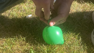 two hands filling a green water balloon with garden hose