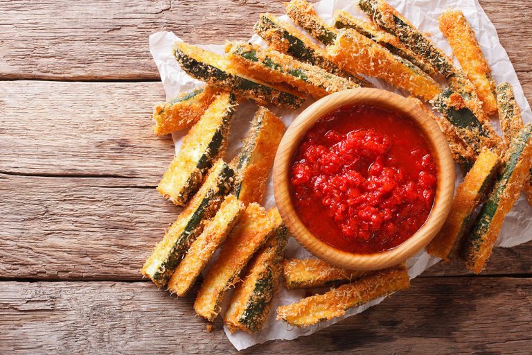 Zucchini fries on a plate with a bowl of tomato sauce in the center.