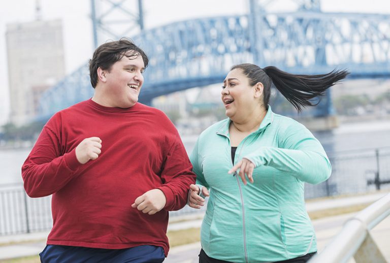 A man and woman running with a bridge in the background.