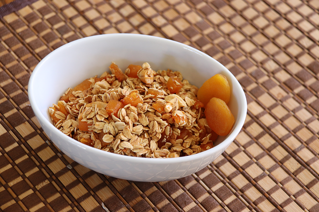 apricot granola in white bowl on checkered tablecloth