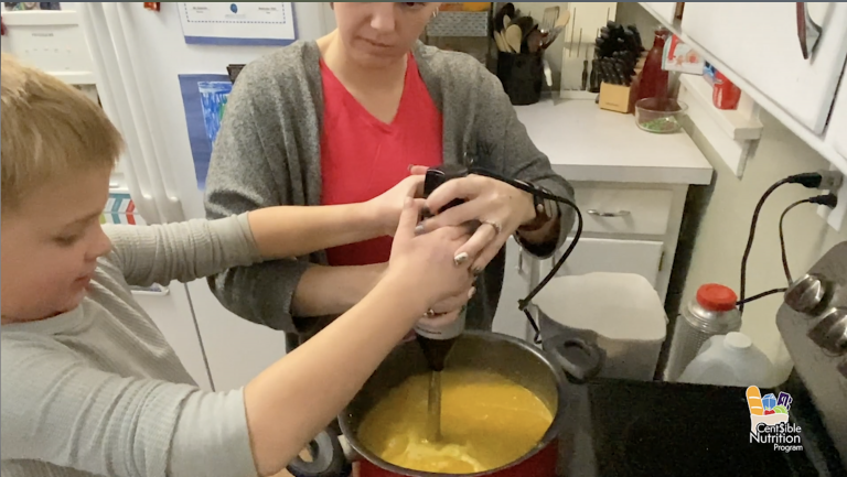 a young boy and woman stir soup together in the kitchen
