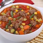 White bowl of beef and vegetable soup with crackers.