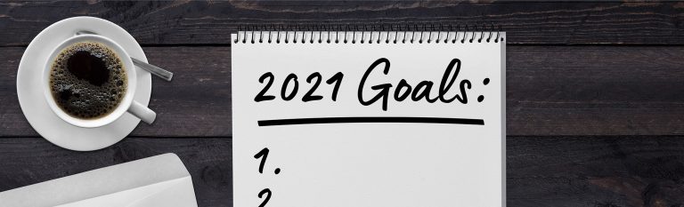 Coffee cup and notebook on table wit the words 2021 Goals written on the paper