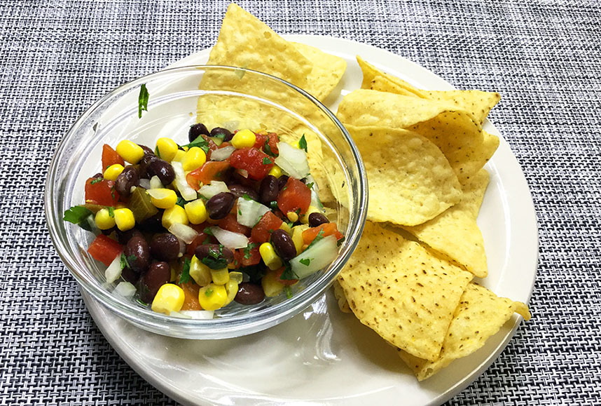 Bean and corn salsa in a glass bowl with yellow corn chips beside it