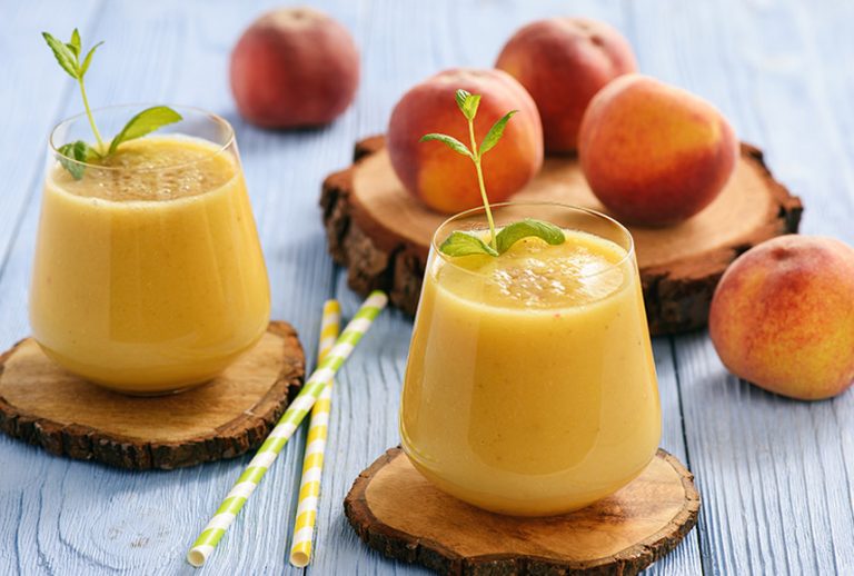 Two peach smoothies in glasses with peaches in the background