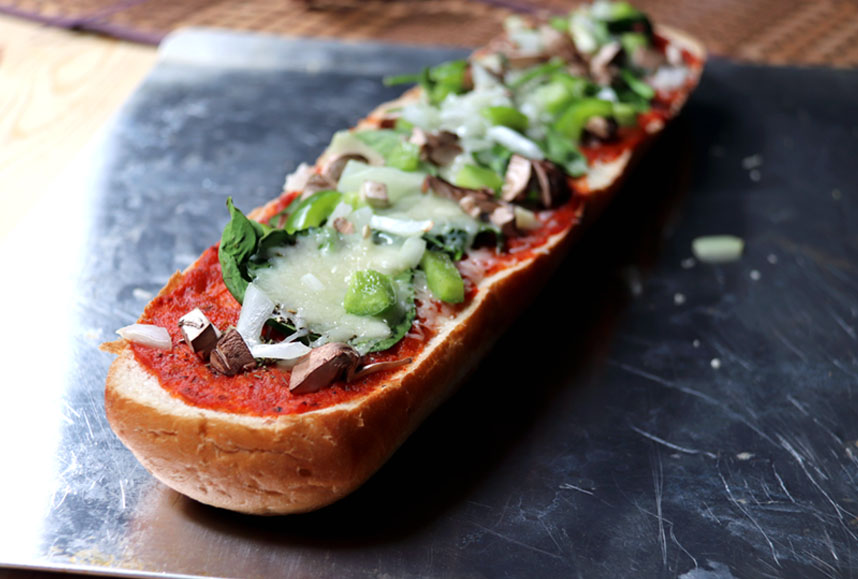 French bread topped with tomato sauce, green vegetables, and cheese