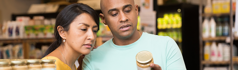 latin american man and woman shopping in grocery store reading label on back of jar