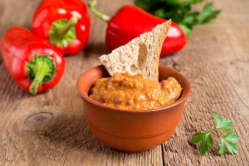 Bowl of roasted red pepper dip with bread. Red peppers decorating background.