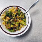 White bowl of beef stew over noodles with broccoli