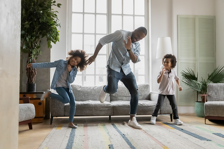 Father dancing with young daughter and son in living room