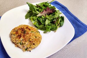White plate with a salmon patty and green salad