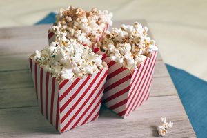Three cups of popcorn in red and white striped boxes on a wooden background. Popcorn has different kinds of spices on it.