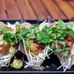 Fish tacos with shredded cabbage, tomatoes, and cilantro on corn tortillas and a side of lime