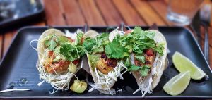 Fish tacos with shredded cabbage, tomatoes, and cilantro on corn tortillas and a side of lime