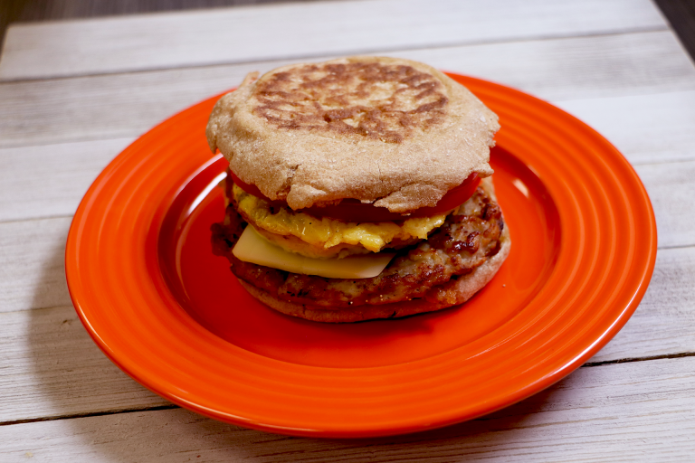 Tasty breakfast sandwich on whole wheat english muffin with pork patty, egg and cheese on plate, ready to eat.