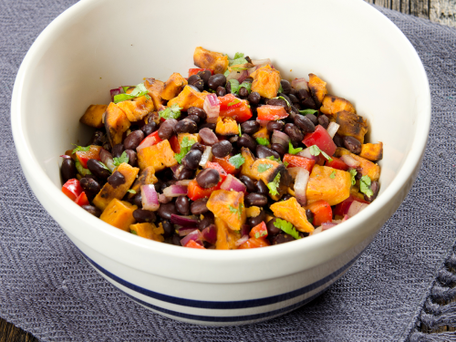 White bowl of black beans, sweet potatoes, peppers, and cilantro tossed together