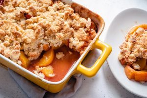 Ceramic baking dish of peach crisp with a golden brown topping.