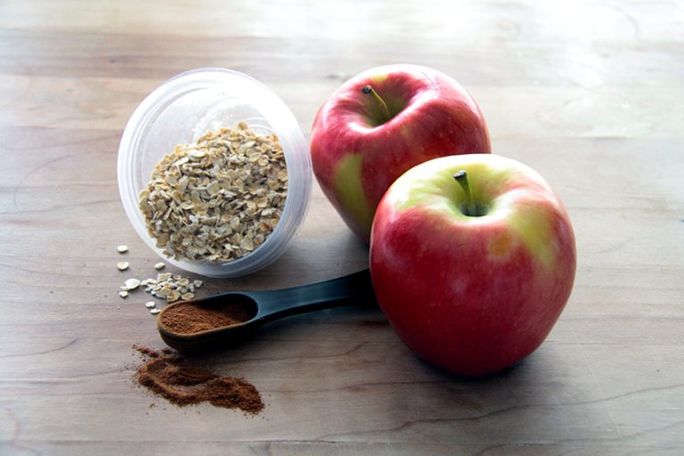 Two red apples on a wooden counter top with oats and cinnamon