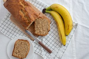 Loaf of banana bread on a cooling rack with bananas and a bread knife