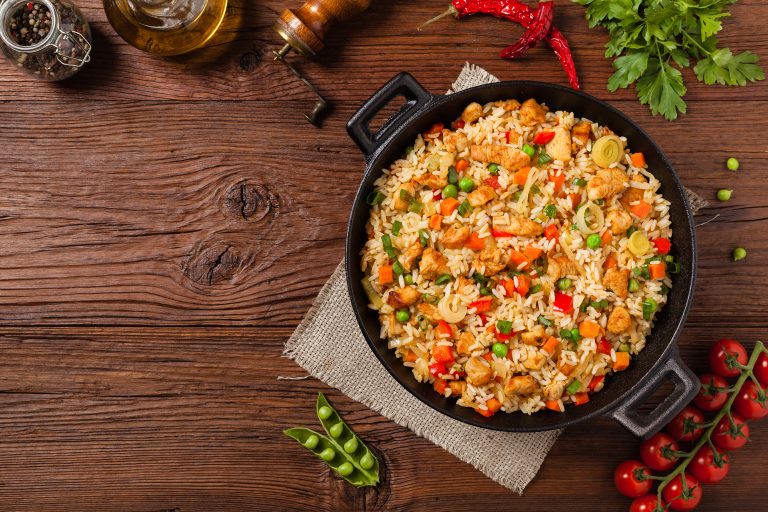 Iron skillet of fried rice and vegetables on a wooden background
