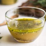 Glass bowl of vinaigrette with herbs beside it