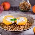 Two halves of a peach with yogurt inside on a bed of granola