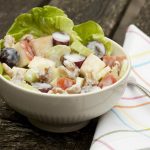 White bowl with various chopped fruit, celery, and nuts in a lettuce cup