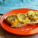 White fish topped with lemon and green herbs on an orange plate