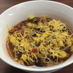 taco soup in white bowl, topped with cheese
