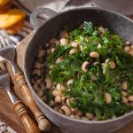 Dish of collard greens, black eyed peas, and corn bread in a rustic pot