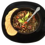 Bowl of soup make with Black-eyed Peas, Chopped Ham Celery Carrot White Onion, Spoon and Crackers over white background