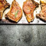 Four pork chops with spices on a baking sheet. On rustic background.