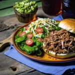 Pulled pork on a bun next to a green salad with tomoatoes