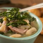 Green bowl of brothy white beans, greens, and ham